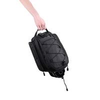 Hand holding the black Corsino Adventure 12L portable bike cargo bag by its top handle, highlighting the rugged 32x18x21cm construction and convenient off-bike transport