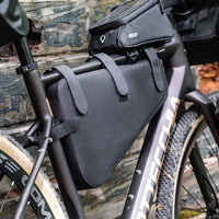 Black bike frame bag attached to a gravel bike frame, made of waterproof 840D Nylon TPU. Dimensions: 39.5x6x23/10 cm, weight: 330g. Features a 5-strap fixation system for stability, a 3-layer support structure to maintain shape under load, and is both waterproof and scratch-resistant.