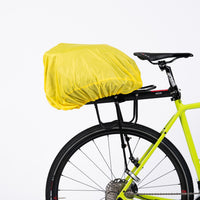 The Corsino Quest 17L trunk cargo bag securely mounted to a bicycle rack, fully protected by the included yellow rain cover to keep cycling essentials dry during wet weather rides