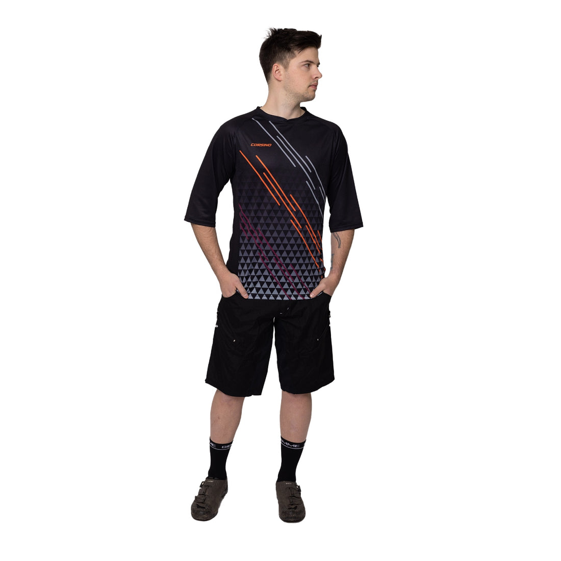 A mountain biker fully geared up in the black Corsino Lines 3/4 Sleeve MTB Jersey. The action-ready comfort fit and protective sleeve length offer the perfect balance of trail durability and cooling performance for aggressive gravity riders